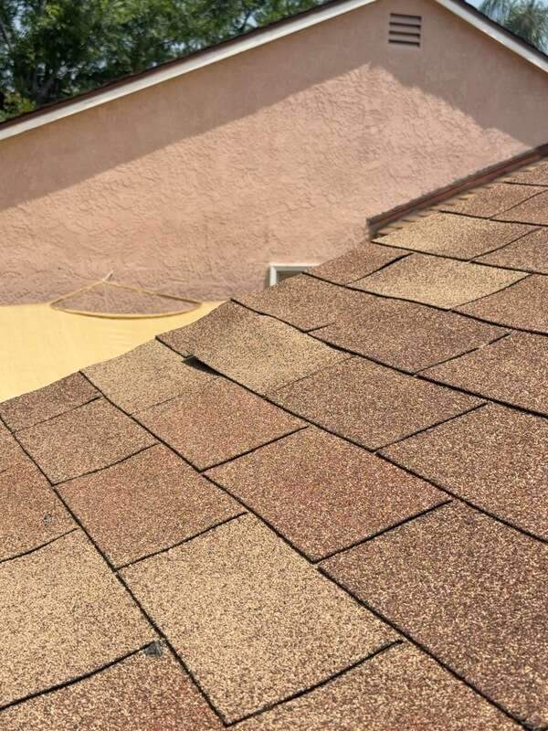 Close view of tan-brown overlapping shingles beside a peach-colored gable wall with a small vent