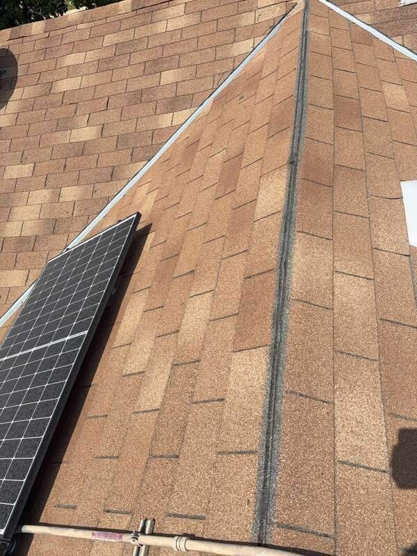 Brown shingle roof ridges and valleys next to part of an existing solar panel.