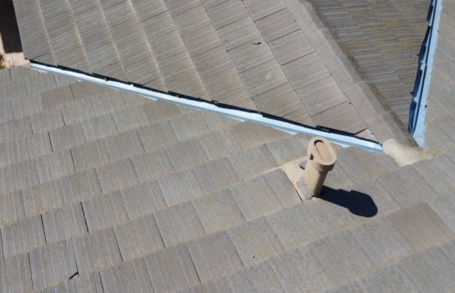 Gray flat-profile tile roof with exposed metal valley channels and a vent