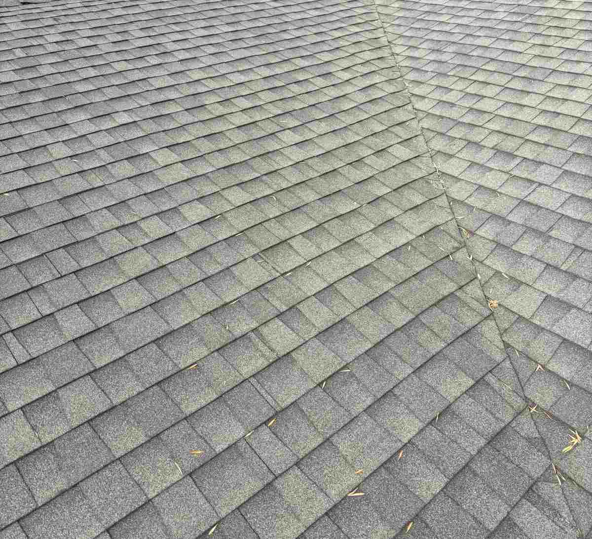 Close view of weathered gray shingles meeting along a roof valley with a few fallen leaves