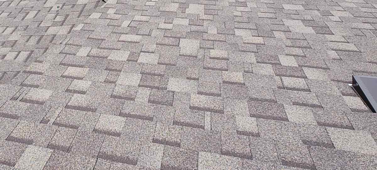 Close view of a gray-taupe shingle field with part of a low-profile roof vent.